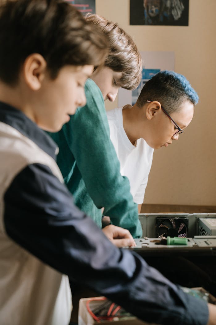 Three teenagers engrossed in assembling computer components indoors.