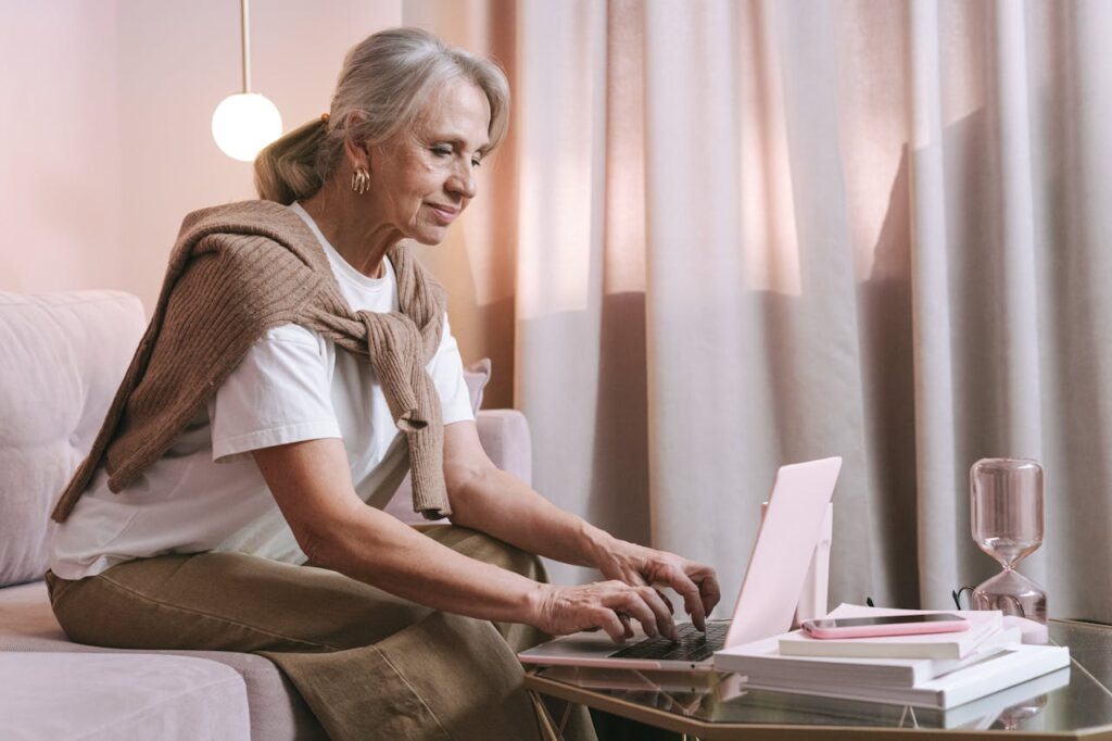 An elderly woman sits comfortably indoors using a laptop, highlighting modern technology use among seniors.